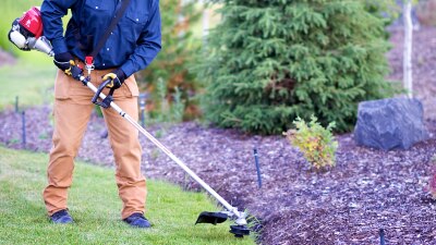 Wide, waist-down view of a gardener trimming the edge of a lawn. 
