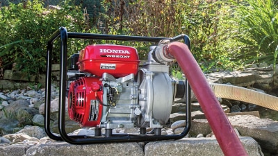 Wide view of transfer pump sitting on stones with hose plugged in. 