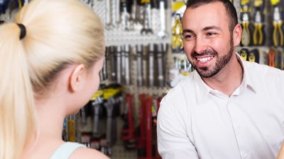 Vue de dos d'une femme blonde face à un homme souriant dans une concession automobile.