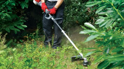 Une personne utilise un outil portatif Honda sur un terrain envahi par les mauvaises herbes et les broussailles.  