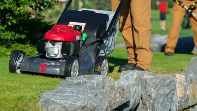 Gros plan d’une tondeuse Honda poussée par un employé en entretien paysager sur une propriété résidentielle de prestige.
