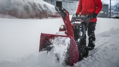 Plan étendu d’une personne qui déblaie une entrée avec une souffleuse à neige devant une grande grange. 