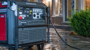 A Honda generator is plugged in and positioned outside a home.  