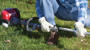 A person is bending down to affix a Honda handheld tool in preparation for use.  