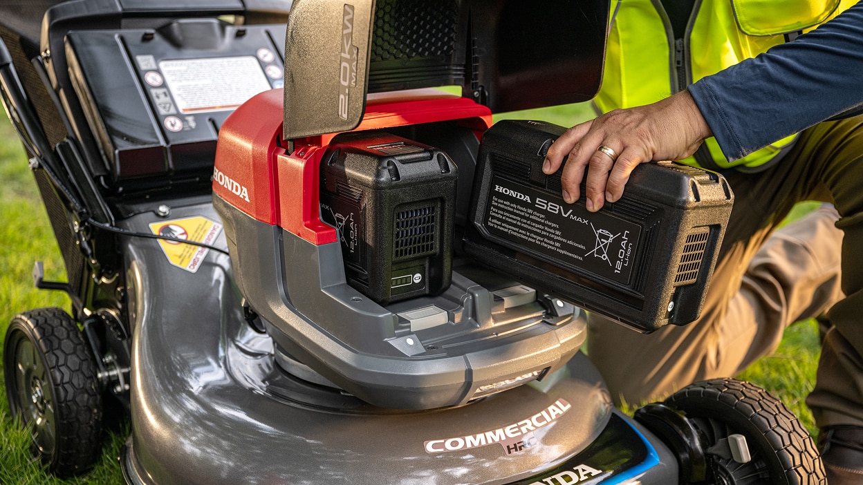 Gros plan montrant l'utilisateur insérant une batterie dans le compartiment à batterie de la tondeuse à batterie.