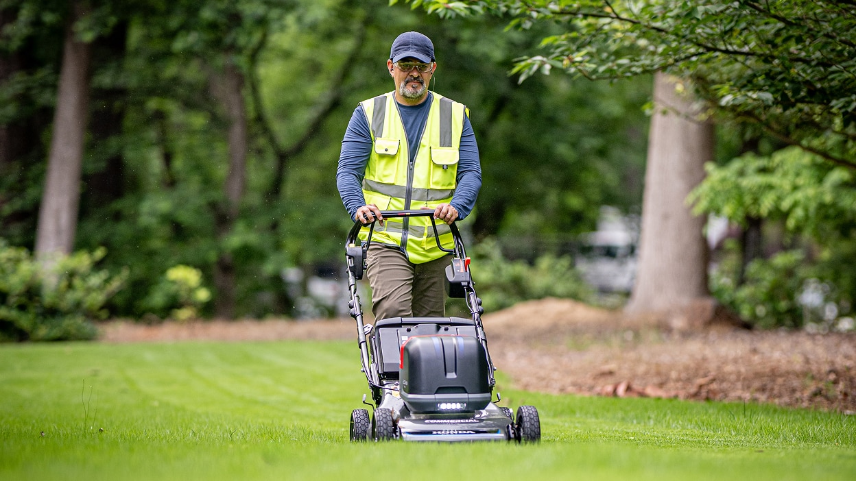 Full frontal view of a person pushing a battery lawn mower in the lawn.