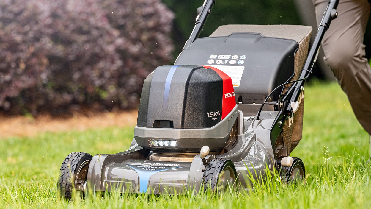 Vue de trois-quart avant gauche montrant une personne poussant une tondeuse à batterie pour tondre la pelouse .