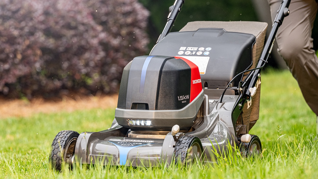 View from three-quarter front left showing a person pushing a battery lawn mower to mow the lawn.