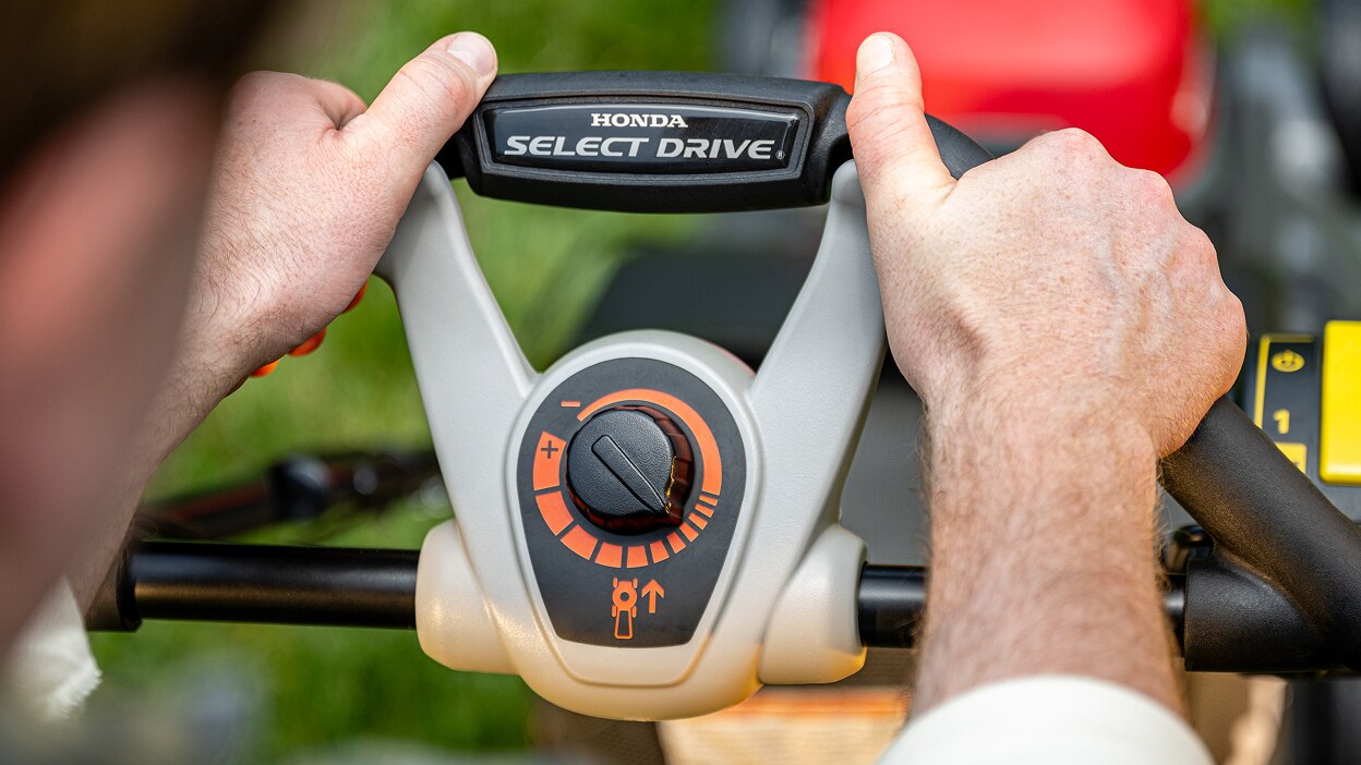 Gros plan des mains d'une personne tenant la poignée de la tondeuse à gazon à batterie. 