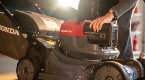 Gros plan montrant l'utilisateur insérant une batterie dans le compartiment à batterie de la tondeuse à batterie. 