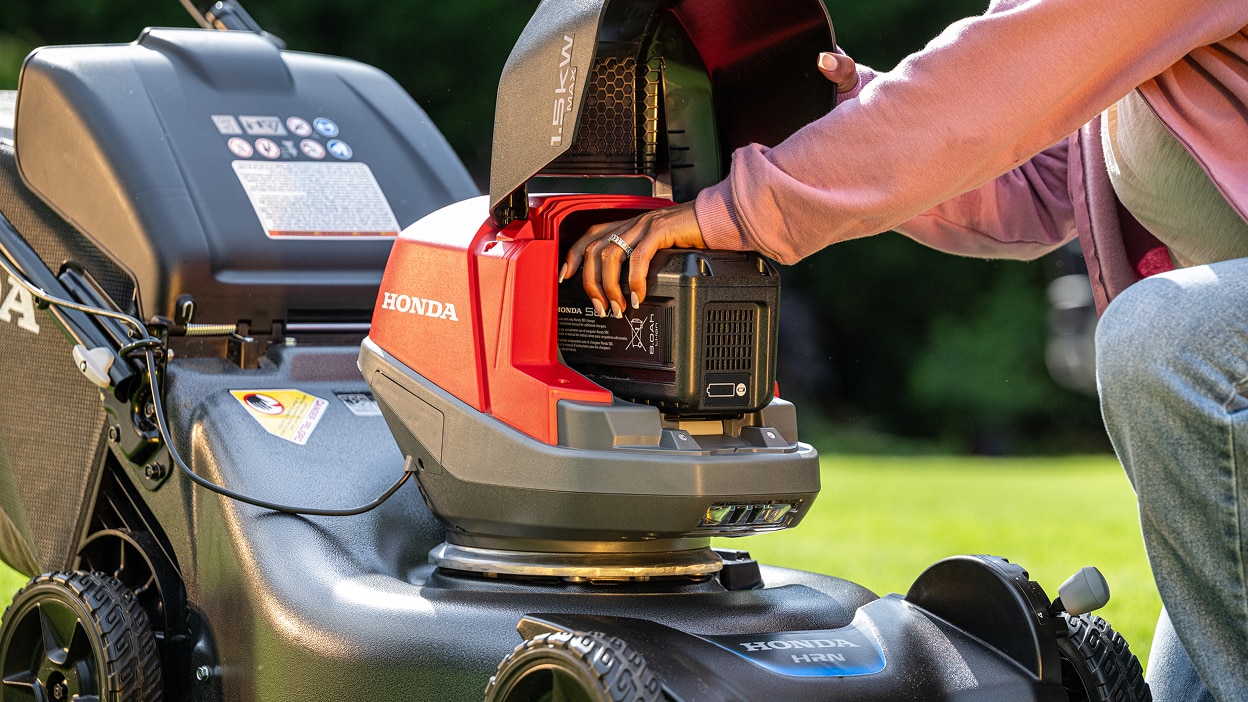 Close up showing the use inserting the battery into the battery lawn mower battery bay.