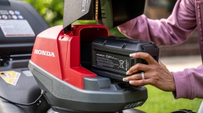 Gros plan montrant l'utilisateur insérant une batterie dans le compartiment à batterie de la tondeuse à batterie. 