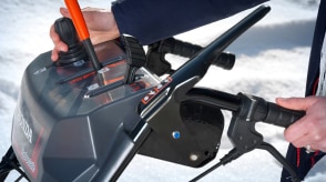 Closeup of a man's hands using the electronic chute joystick control on the handlebar-mounted console on a snowblower.  